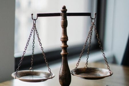 Bronze scales of justice sit on a table against a blurred window background.