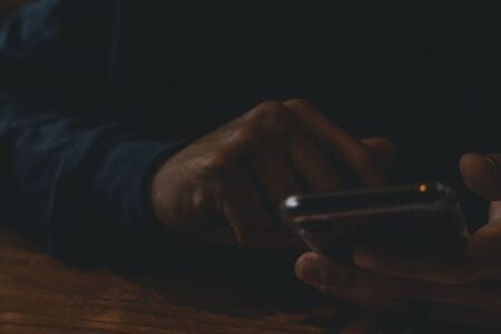 Hands hold and interact with a smartphone on a dark wooden surface.
