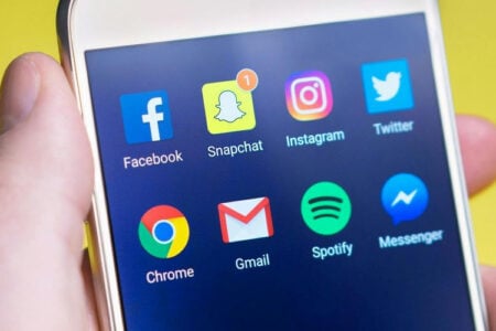 Hand holding smartphone displaying social media and communication app icons.