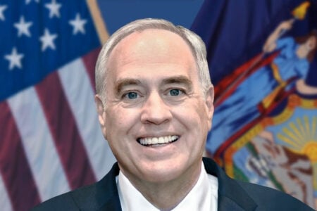 New York State Comptroller Thomas DiNapoli smiles in front of American and New York flags.