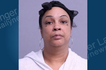 Woman in a dark headscarf, light hoodie, and hoop earrings with smudged eye makeup, facing camera in a mugshot.