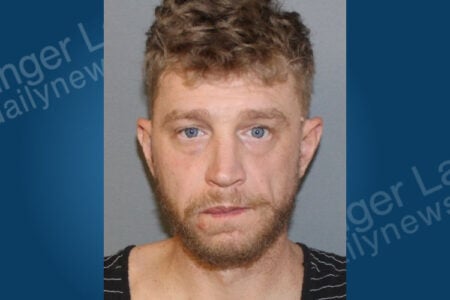 Mugshot of a blond man with a beard against a neutral background.