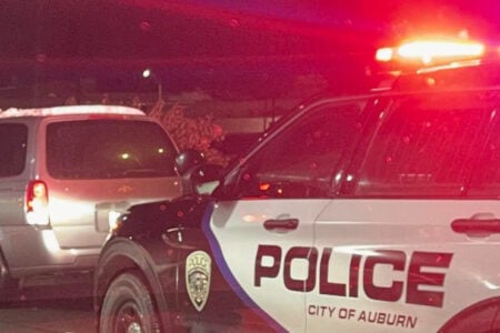 Auburn Police car with lights flashing behind a parked minivan on a street at night.