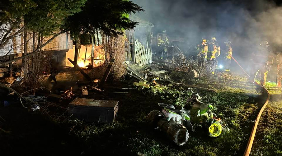 Firefighters battle a house fire at night in the Finger Lakes region, smoke and flames visible.