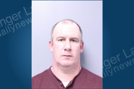 A man with short graying hair, blue eyes, and a maroon shirt poses for a mugshot.