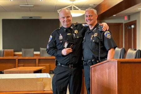 Two Ontario County Sheriff's Office deputies pose together in uniform indoors, one holding a badge.