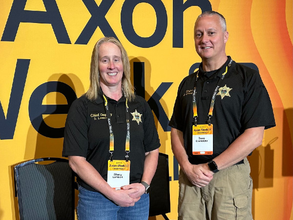 Stacy Lambrix and Dave Cincinello, in law enforcement uniforms, pose at an Axon Week event.