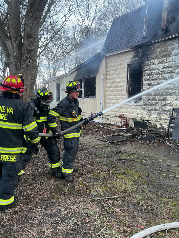 Geneva firefighters extinguish a house fire, spraying water on the charred building.