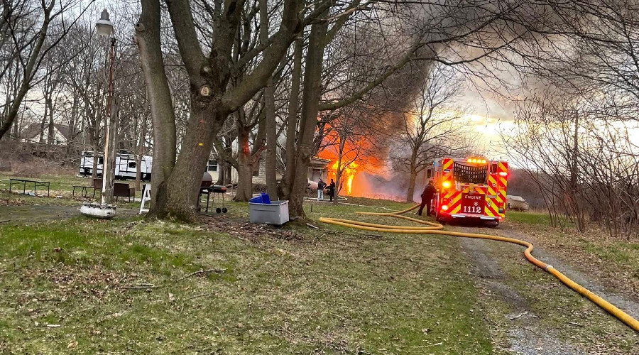 Firefighters battle a house fire in a yard with engine 1112 visible and flames erupting from the home.