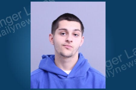 Mugshot of a young man with short dark hair and stubble, wearing a blue hoodie, against a plain background.