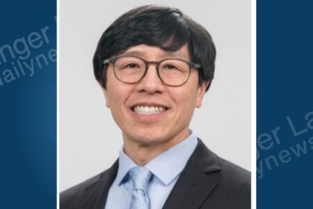 Headshot of a smiling man with glasses, wearing a suit and tie, against a neutral background.