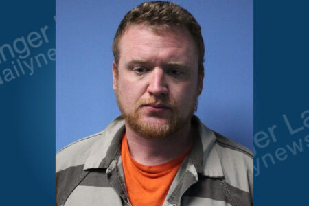 Mugshot of a man with reddish hair and beard, wearing a striped jail uniform, against a blue background.