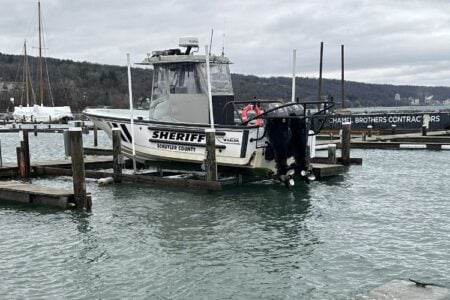 The Schuyler County Sheriff's boat sits raised on a boat lift in a marina on a cloudy day in the Finger Lakes.