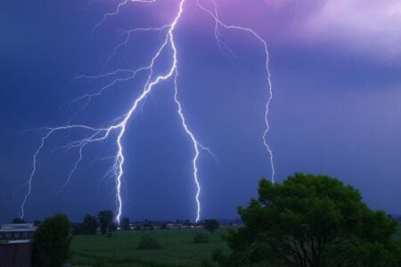 Lightning strikes over a rural area in the Finger Lakes, with a field and some buildings visible.