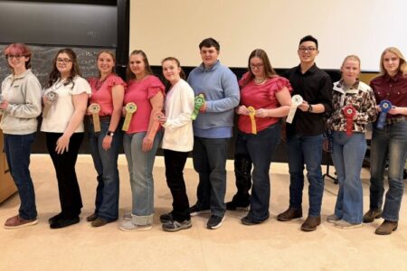Ten students standing in a line, proudly displaying their award ribbons in a classroom.