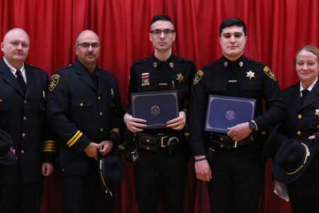 Five Finger Lakes County Sheriff's Office personnel stand with awards in front of a red curtain.