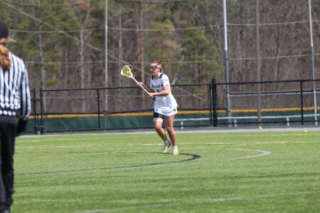 Keuka College lacrosse player runs with her stick on the field as a referee walks nearby.