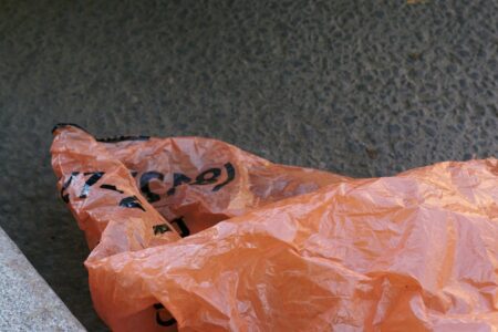 A crumpled orange plastic bag with black lettering sits on a gray concrete surface.
