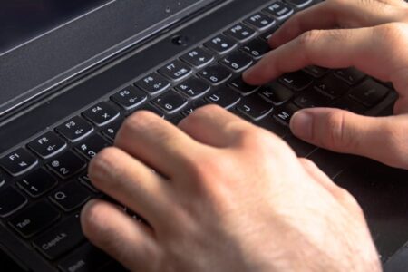 Close-up of hands typing on a black laptop keyboard. (53 characters)