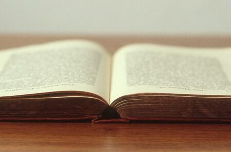 Open, aged book with dark red cover lies on a wooden surface, pages spread to display text.