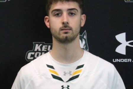Young man with a short beard posing in a white Keuka College jersey against a dark background with logos.