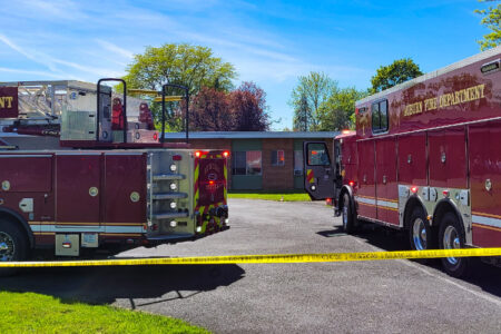 Auburn Fire Department ladder truck and engine parked at an incident scene in front of a building, marked by caution tape.