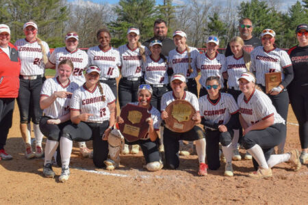 Corning Softball team and coaches in uniform pose on a dirt field, holding championship plaques.