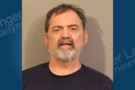 A bearded man in a dark t-shirt faces the camera for a mugshot against a plain background.