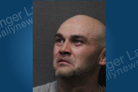 Man with shaved head and beard stubble, wearing a gray shirt, looks up and to the left in a booking photo.