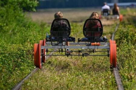 Two people pedal a tandem rail bike on a grassy railway track in the Finger Lakes.