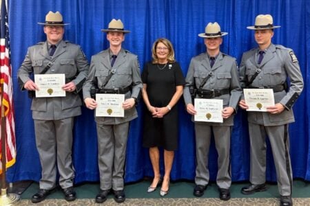 Four New York State Police officers in uniform display their citations, posing with a woman against a blue curtain.