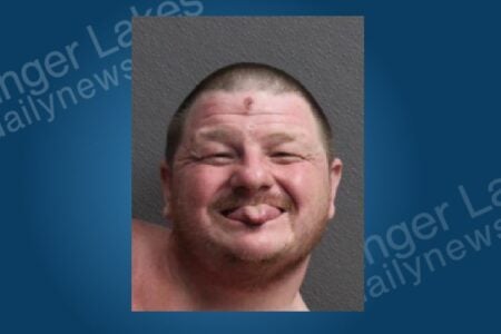 A man in a mugshot smiles with squinted eyes and sticks his tongue out at the camera.