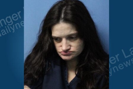 Woman with long dark hair, looking down with pursed lips, against a plain blue background.