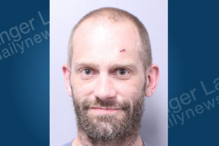 Mugshot of a bearded man with a small cut on his forehead, looking directly at the camera.