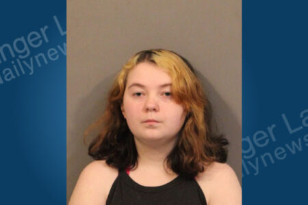 Young woman with long, two-toned blonde and brown hair looks straight ahead in a police mugshot.