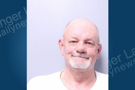 Bald man with a white goatee and white t-shirt faces forward in a mugshot against a plain light background.