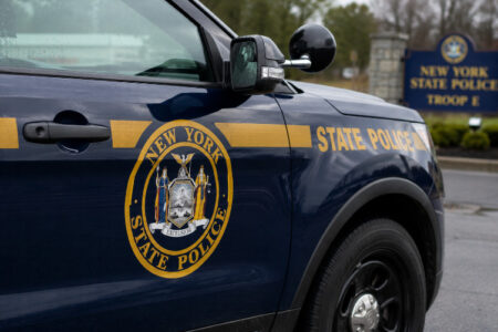 NY State Police vehicle with its emblem and 'STATE POLICE' text, parked in front of the Troop E station sign.