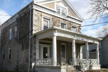 Two-story house with textured facade, dormant vines on the left, white columned porch, and address 495.