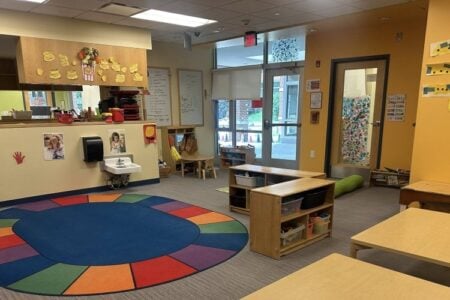 Bright, colorful, and empty preschool or daycare classroom with a rainbow rug, child-sized furniture, and decorated walls.