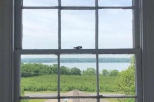Elevated view from a weathered multi-pane window showing a Finger Lake, green landscape, and a shingled roof.