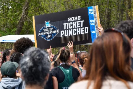 Crowd holds oversized 2026 NCAA DIII Rowing Championships 'Ticket Punched' sign outdoors near a shell.