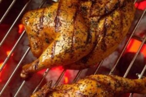 Two golden brown seasoned chicken halves grilling over hot red coals.