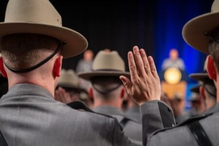 NY State Trooper recruits in grey uniforms and tan hats raise hands during swearing-in.