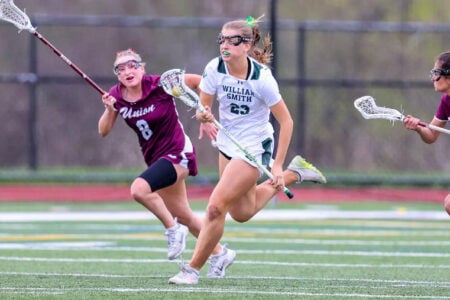 William Smith's #23 runs with the lacrosse ball, pursued by two Union players on the field.