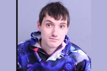 Man with dark hair and light mustache wears a purple galaxy hoodie, looking at the camera against a plain background.