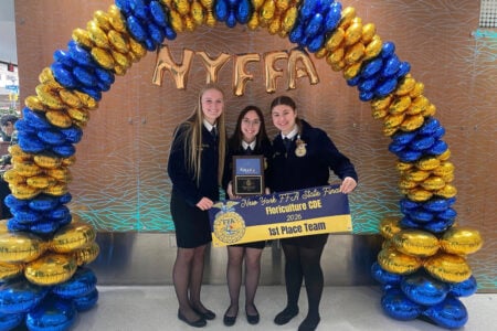Three smiling NYFFA members in uniform hold their 1st Place Floriculture CDE award plaque and banner.