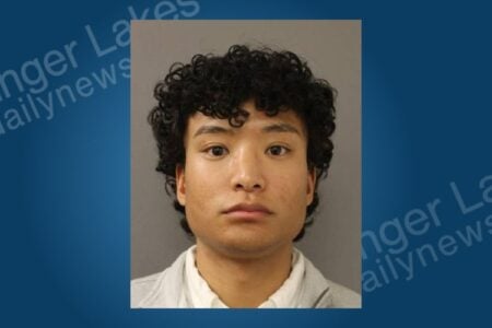 Young man with dark curly hair and a neutral expression in a police mugshot against a plain background.