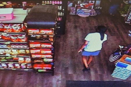 Person in a light shirt and blue shorts walks through a store aisle lined with snack shelves, captured by overhead camera.