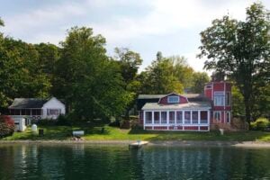 Red "Sunny Point" house with a tower and a white cottage on a Finger Lakes shore, surrounded by green trees.