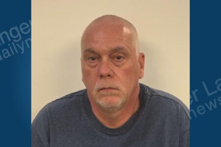 Bald white man with a gray goatee looking at the camera against a plain background, wearing a dark blue shirt.
